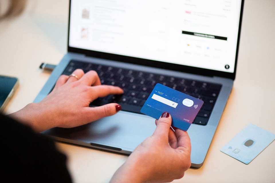 Laptop menampilkan halaman checkout, kartu kredit di tangan siap membayar
